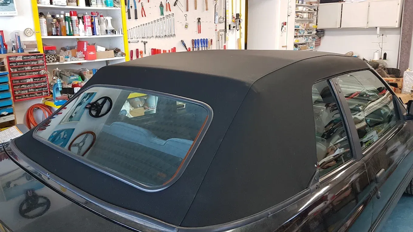 Capote nera nuova su un'auto cabriolet scura, vista da dietro, con il banco da lavoro sullo sfondo.