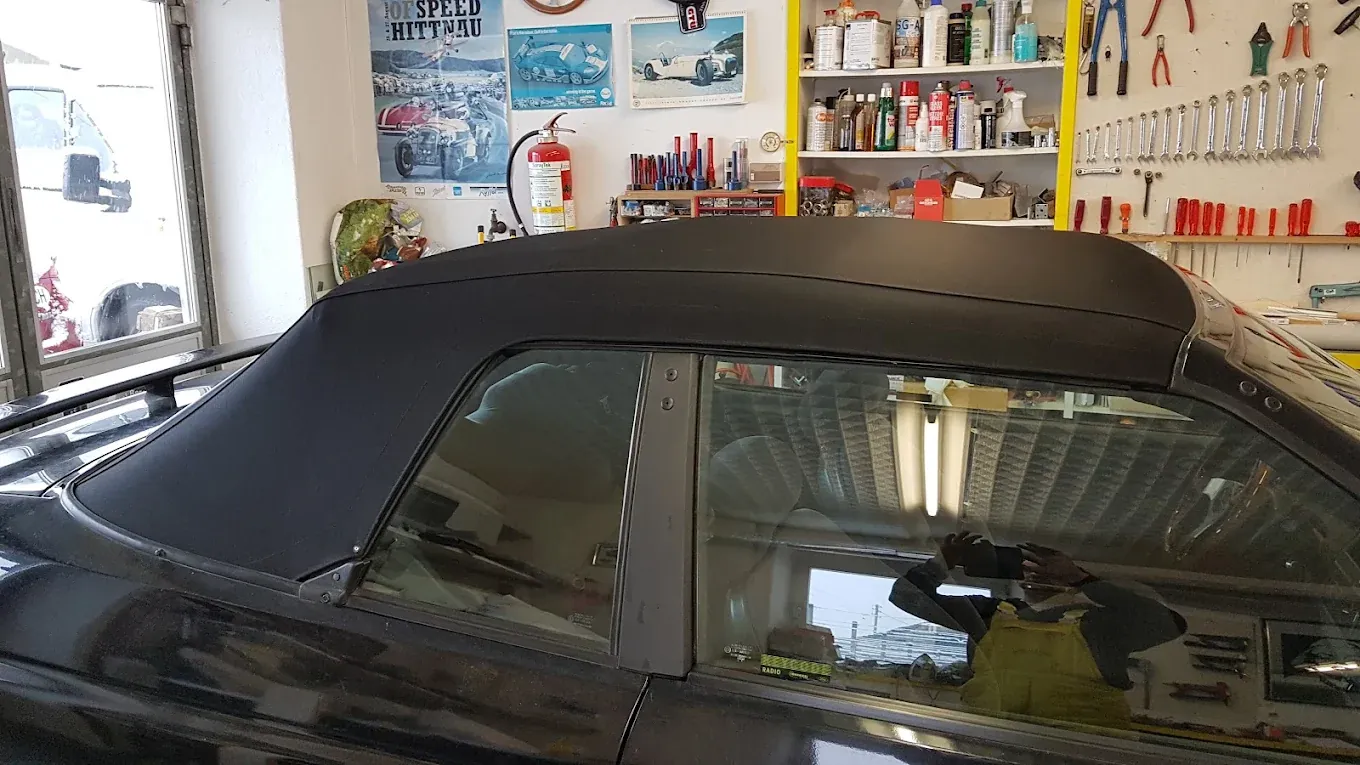 Capote nera montata su un'auto cabriolet scura, vista di profilo in laboratorio.