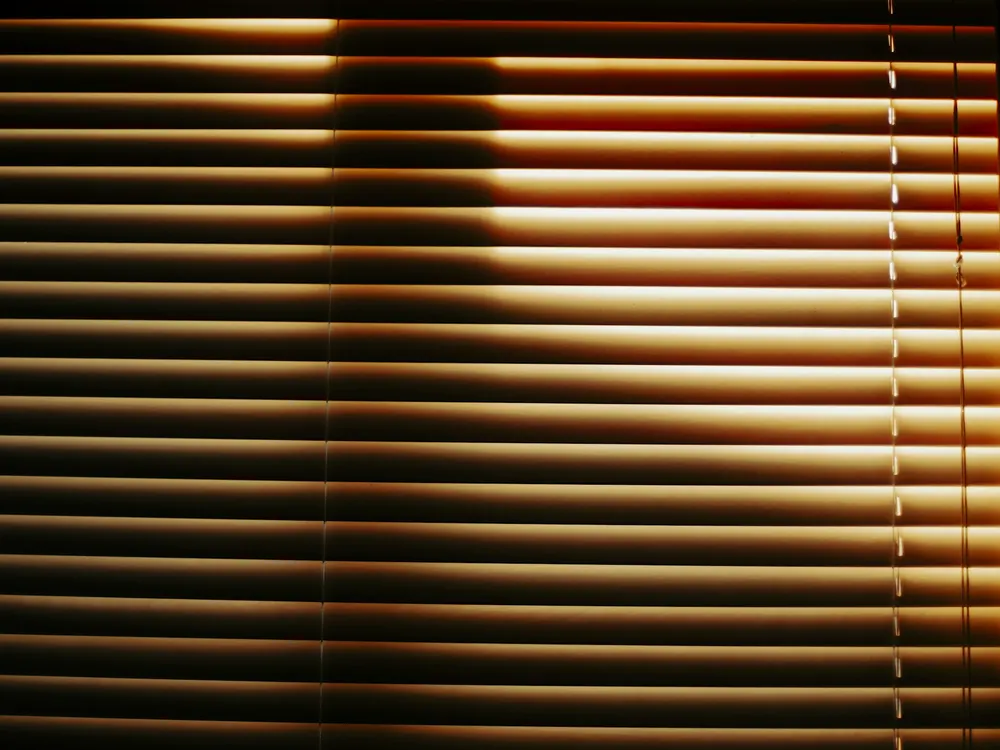 Lamelle orizzontali di una tenda veneziana attraversate dalla luce del sole.